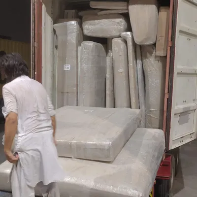 A customer overseeing the packing of wrapped furniture and mattresses into a container
